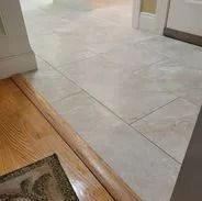 Light tile floor meets wooden flooring with doorway in the background.