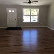 Empty living room with hardwood floors, a window, and a white door.