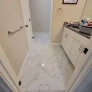 Bathroom with white marble-look floor, white cabinets, and a doorway.