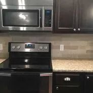 Stainless steel microwave and electric range in a kitchen with dark cabinets and tan countertops.