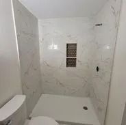 Bathroom with white marble-look tile walls and a white shower base. A small recessed shelf.