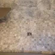 Shower floor with small gray tiles and a metal drain.