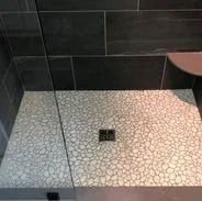 Shower with pebble tile floor, dark gray wall tiles, and a glass door.