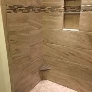 Tiled shower with neutral-toned walls. A mosaic border and built-in shelf are visible.
