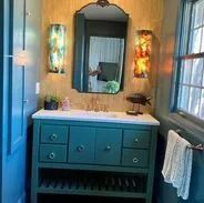 Bathroom with teal vanity, mirror, and sconces.