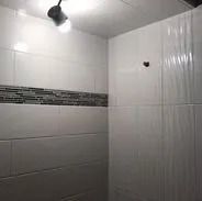 White-tiled shower with accent tiles, lit by a single bulb.