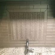 Gray tiled kitchen backsplash with herringbone pattern insert. A faucet is visible at the bottom.