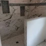 Marble-tiled shower with mosaic accent. Includes built-in shelves, glass wall, and drain.