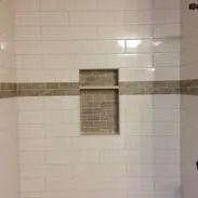 White subway tiled shower wall with a brown tiled band and a recessed shelf.