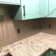 Light brown tiled backsplash with countertop and green cabinet.