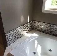 A bathroom with a white bathtub, mosaic tile trim, and gray walls.