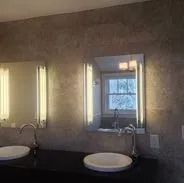 Mirrors and sinks in a bathroom with modern lighting and stone walls.
