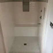 White tiled shower with gray tiled floor, built-in bench, and dark fixtures.
