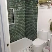 Bathroom with green tiled shower, white toilet, and black and white floor tiles.