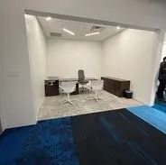 Office space with desk, chairs, and carpet. White walls with blue and grey carpet.