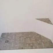 Gray building block pieces on a white surface; one large, irregular shape with a small, triangle piece above.