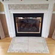 Fireplace with white mantel, black and gold fireplace and beige tile hearth.