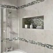 Bathroom shower with light gray tiles, a mosaic tile accent, and a built-in shelf with decor.