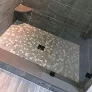 Shower with mosaic tile floor and gray wall tiles, corner shelf.