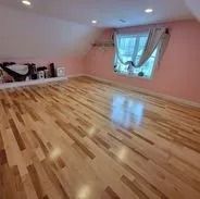 Hardwood floor in an attic room with a window and pink walls.