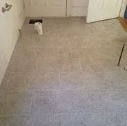 Gray tiled bathroom floor with a toilet pipe and open drain, near a closed white door.