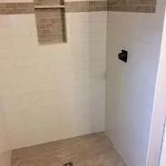 Empty shower with beige floor and white walls, small tile accent strip, and dark faucet.
