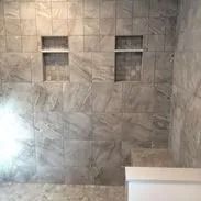Bathroom wall with gray marble-look tiles, two built-in shelving niches, and white accent.