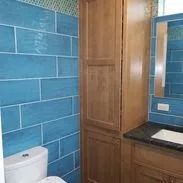 Bathroom with blue tiled walls, wooden cabinet, toilet, and sink.