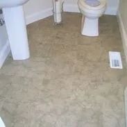 A small bathroom with tan vinyl flooring, a white toilet, and a white sink with a pedestal.