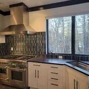 Stainless steel kitchen with range, tiled backsplash, and window overlooking trees.