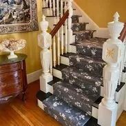 Staircase with floral runner, white balusters, wood banister, and chest of drawers.