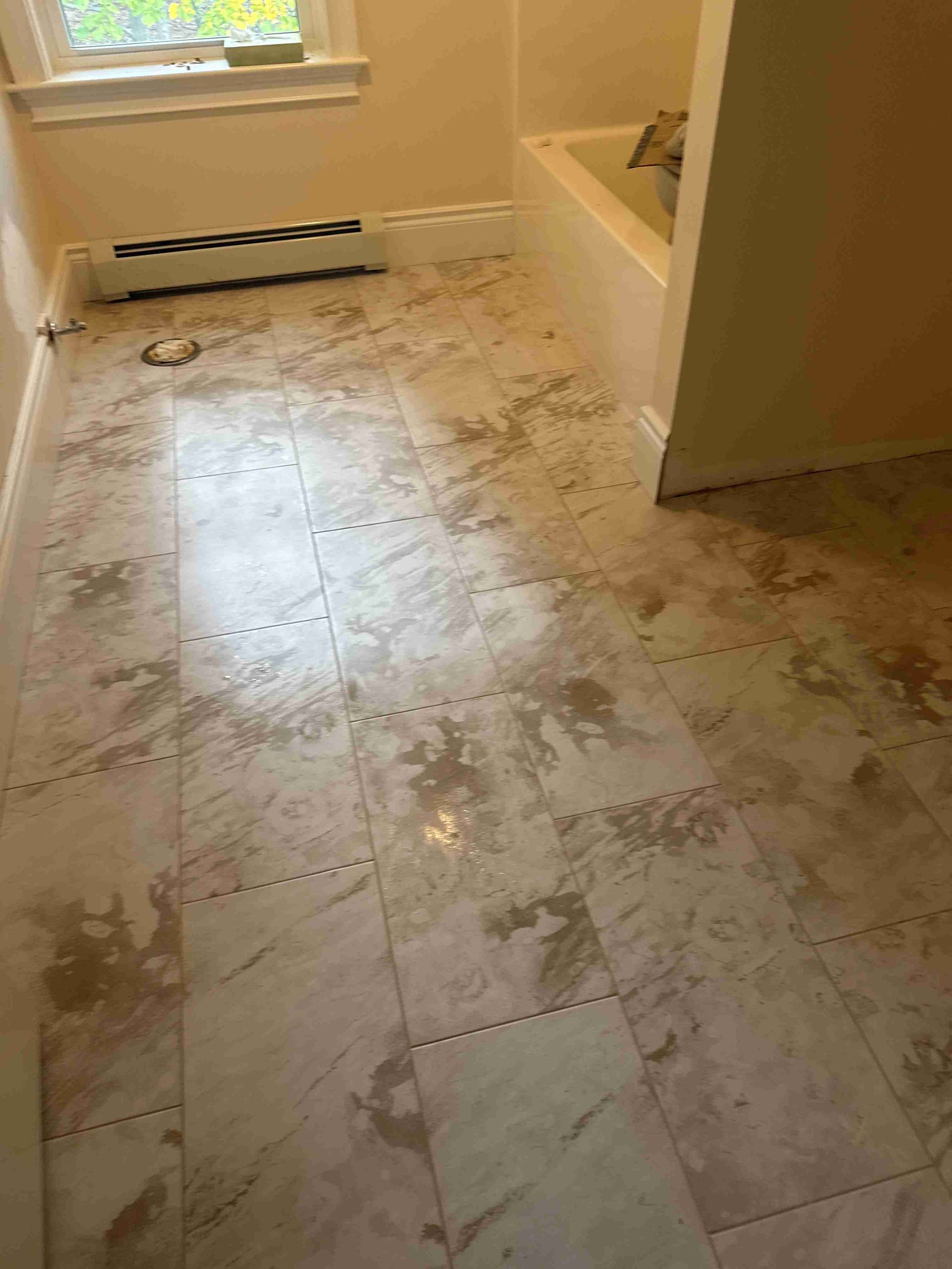 Bathroom floor with beige and white tile, a bathtub, and a radiator.