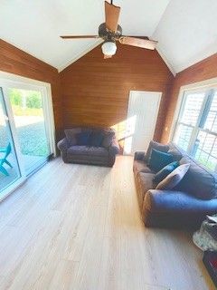 Sunroom with two sofas, wood paneling, and sliding glass door. Pale wood floor.
