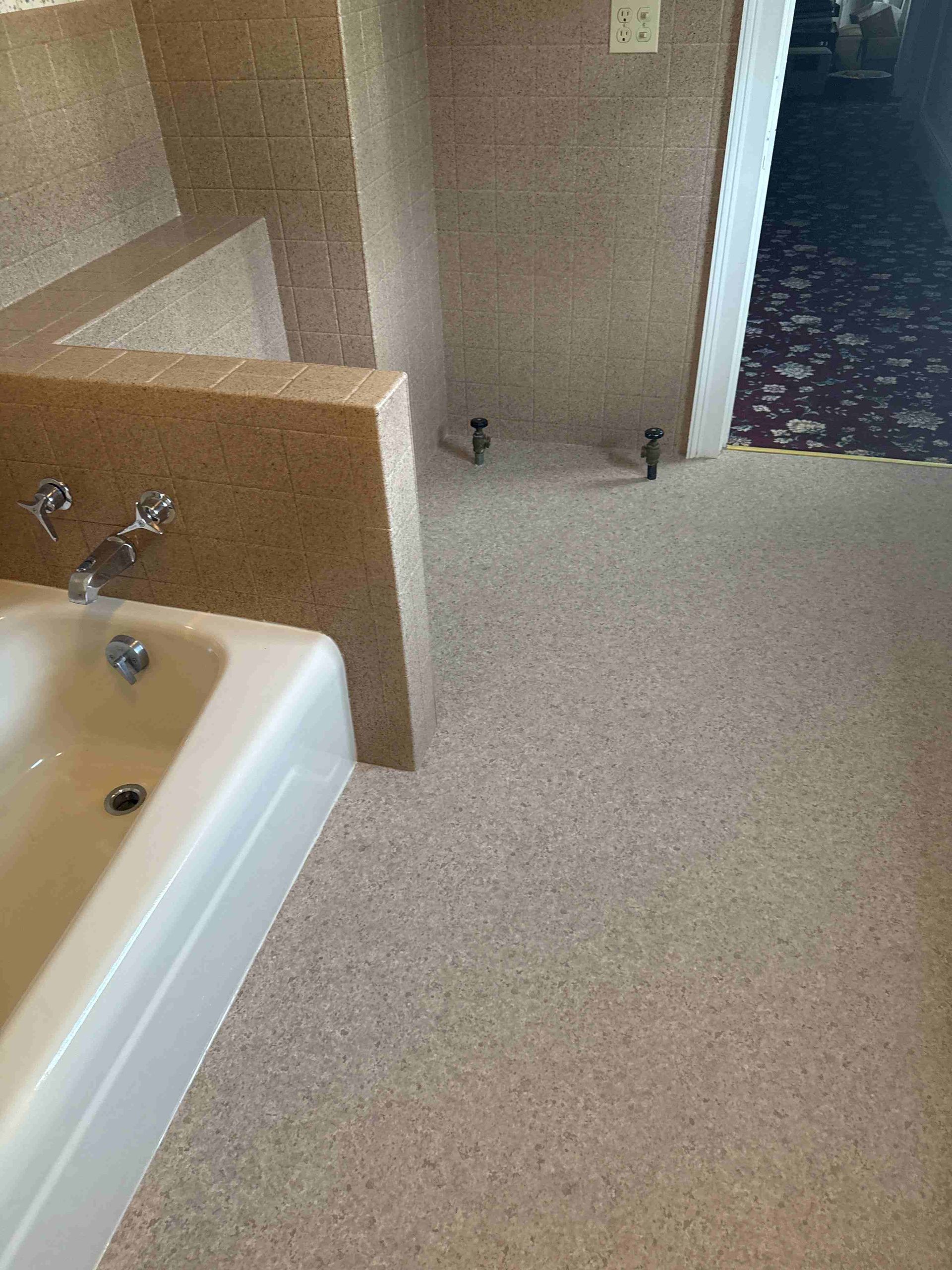 Bathroom with a tub, tiled wall, and speckled floor. The doorway with carpet is visible.
