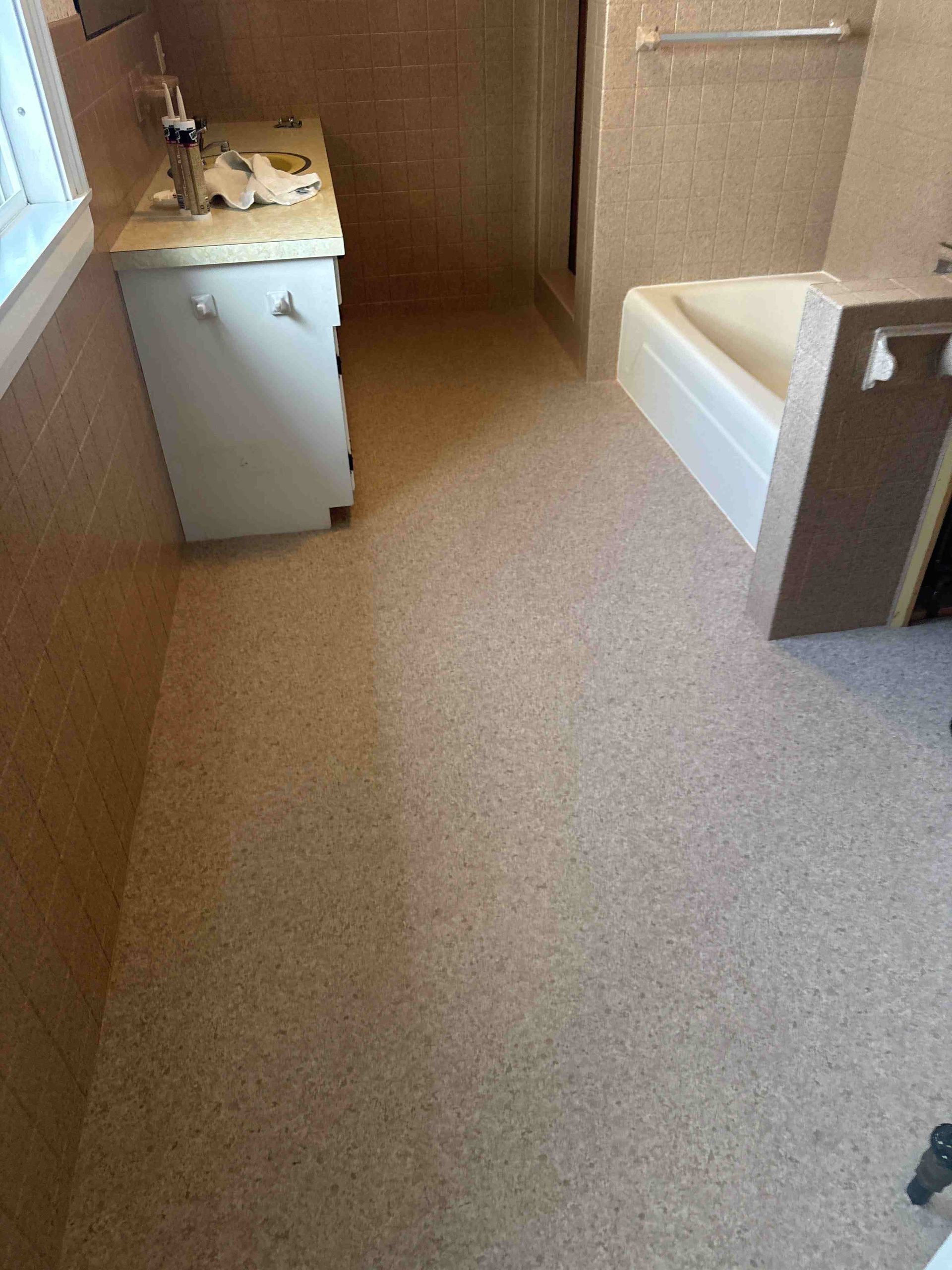 Bathroom with speckled beige flooring, white vanity, tub, and beige tiled walls.