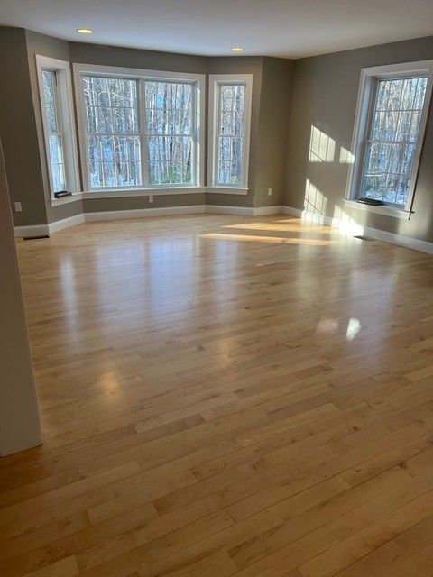 Empty living room with wood floors, large windows, and gray walls.