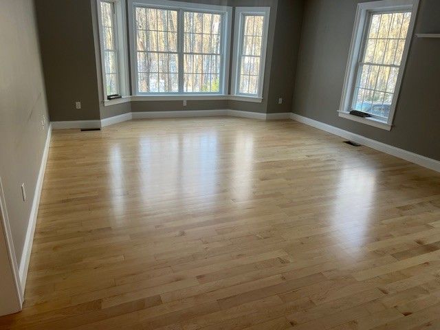 Empty room with shiny, light-colored wood floors and large windows. Walls are gray.