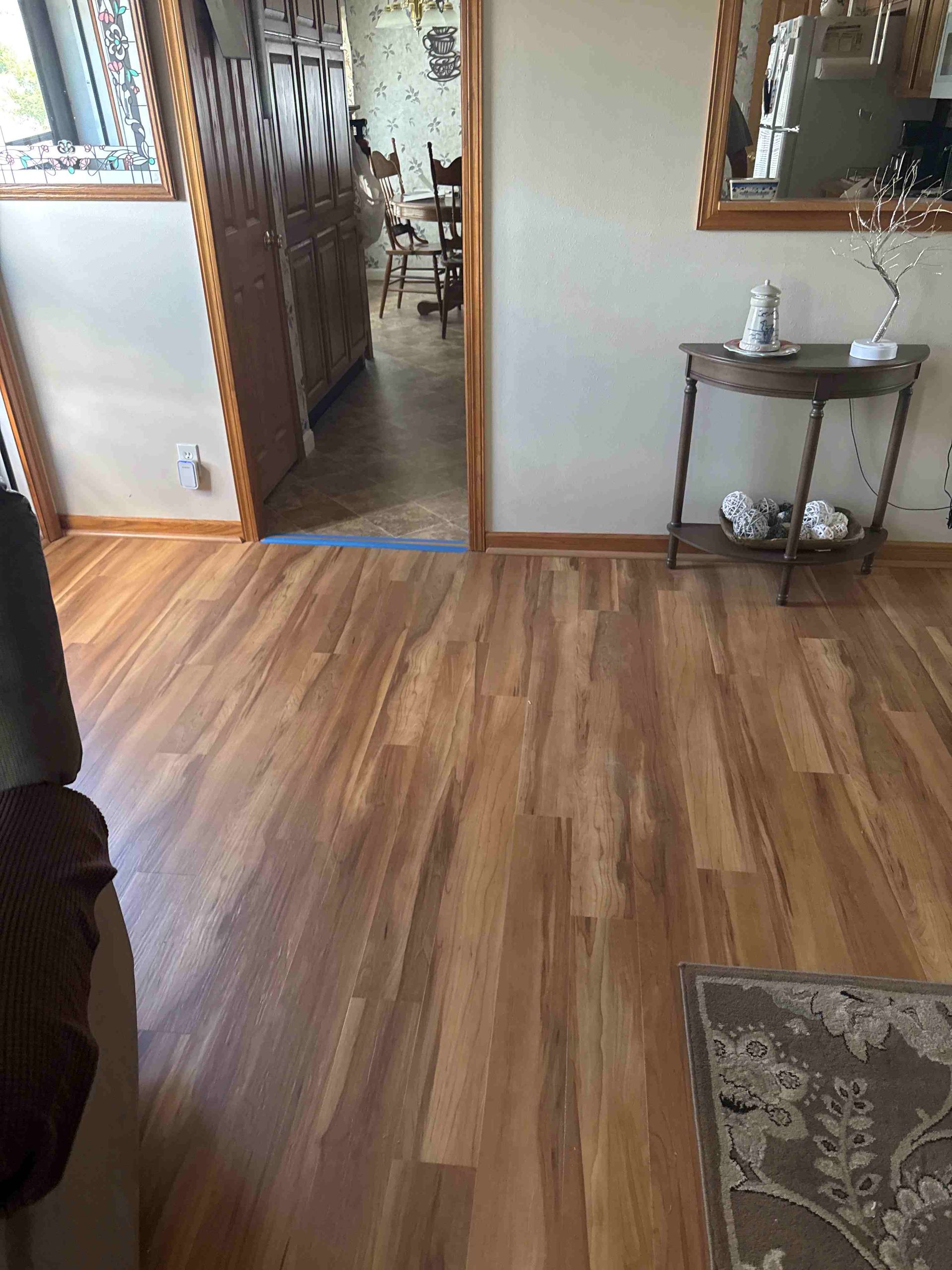 Wooden floors in a living room with an entryway to a dining room and a table with decor.