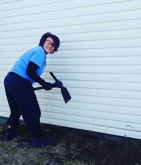 A woman is leaning against a wall holding a shovel