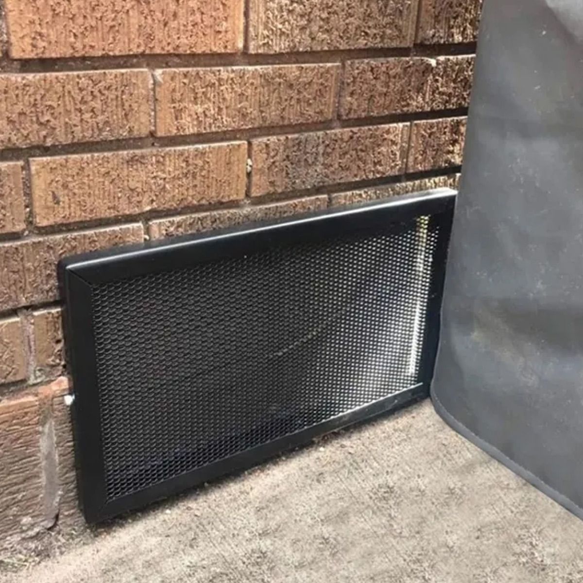 A black screen is sitting on the ground next to a brick wall.