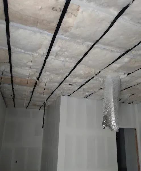 Insulated ceiling with exposed black support strips and hanging silver duct in an unfinished room