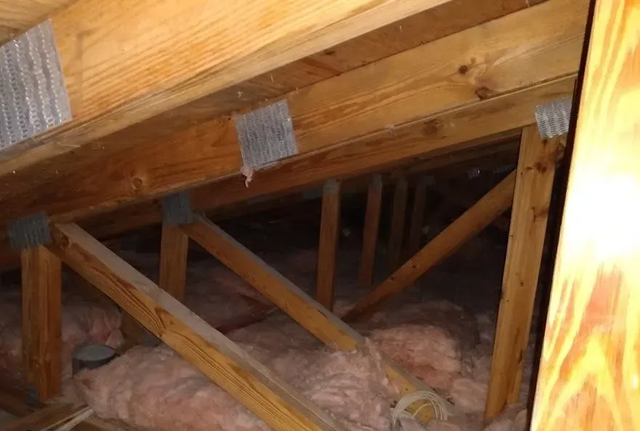 Wooden attic framing with insulation and cross-bracing beams under a sloped roof.