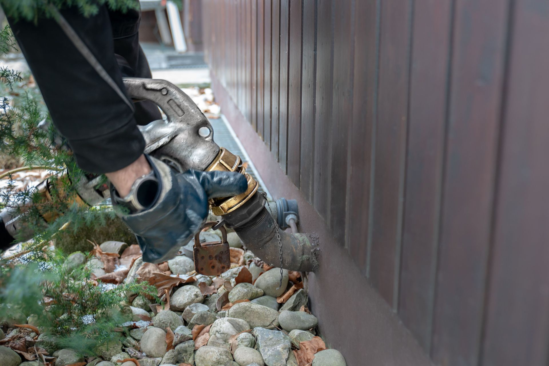 Person fueling a tank near a brown wall with a fuel nozzle; rocks and foliage surround it.