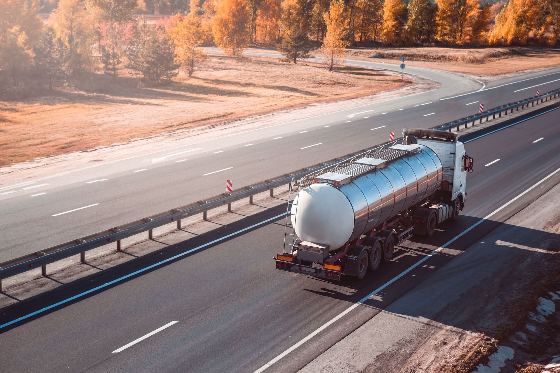 Tanker truck driving on a highway with fall foliage in the background.