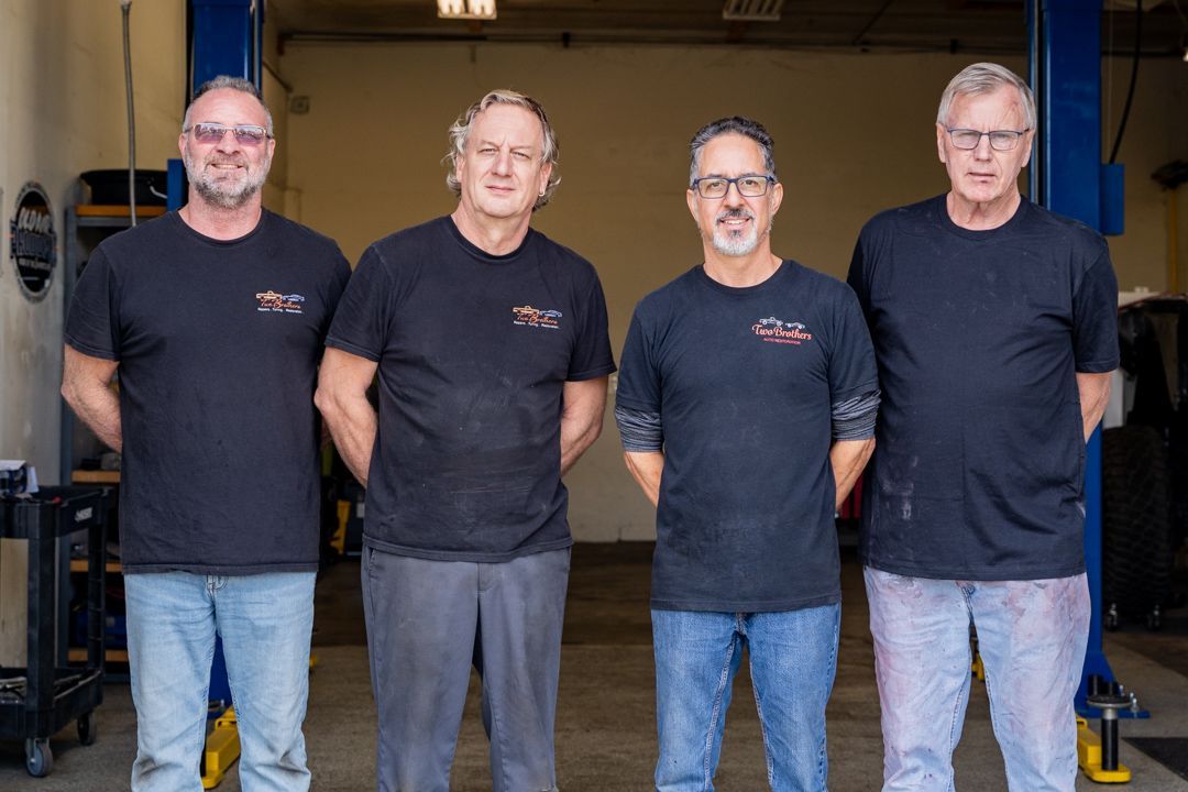 Four men in a garage, wearing black shirts, stand side-by-side.