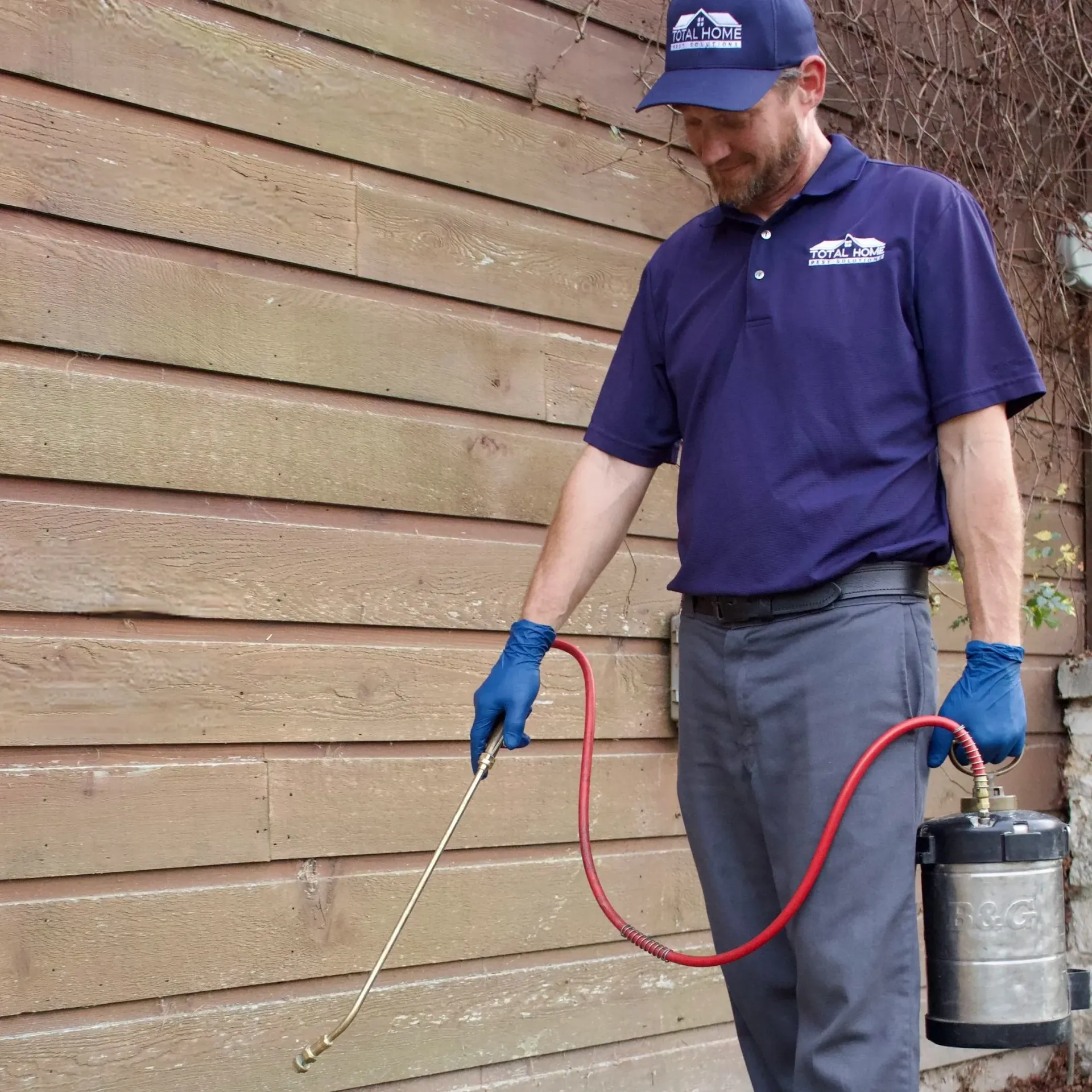 Man in blue spraying insecticide on wooden siding.