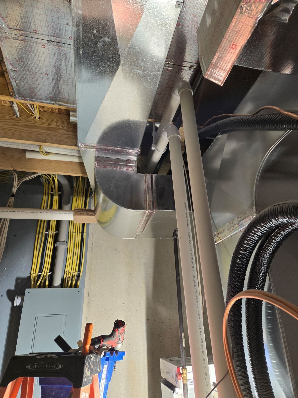 Ceiling HVAC ductwork and exposed wiring above a utility space, with pipes and cables visible.