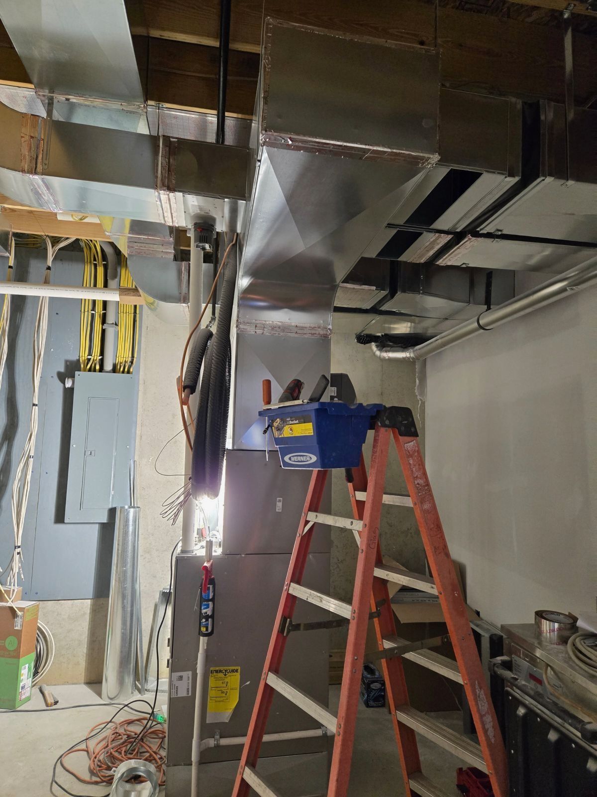 Construction site with ladder under exposed ceiling ducts and hanging wires in a room.
