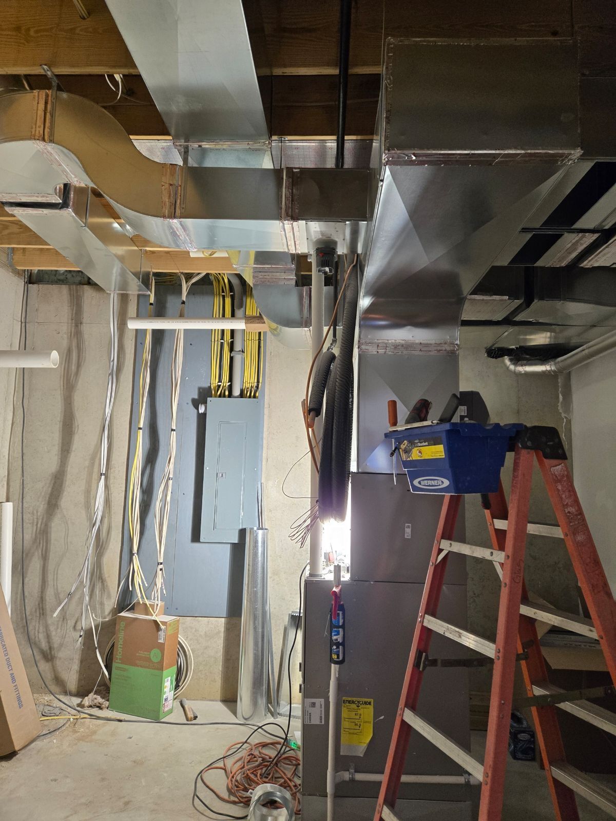 Construction site with exposed ceiling ducts, hanging wires, and ladders in an unfinished room.