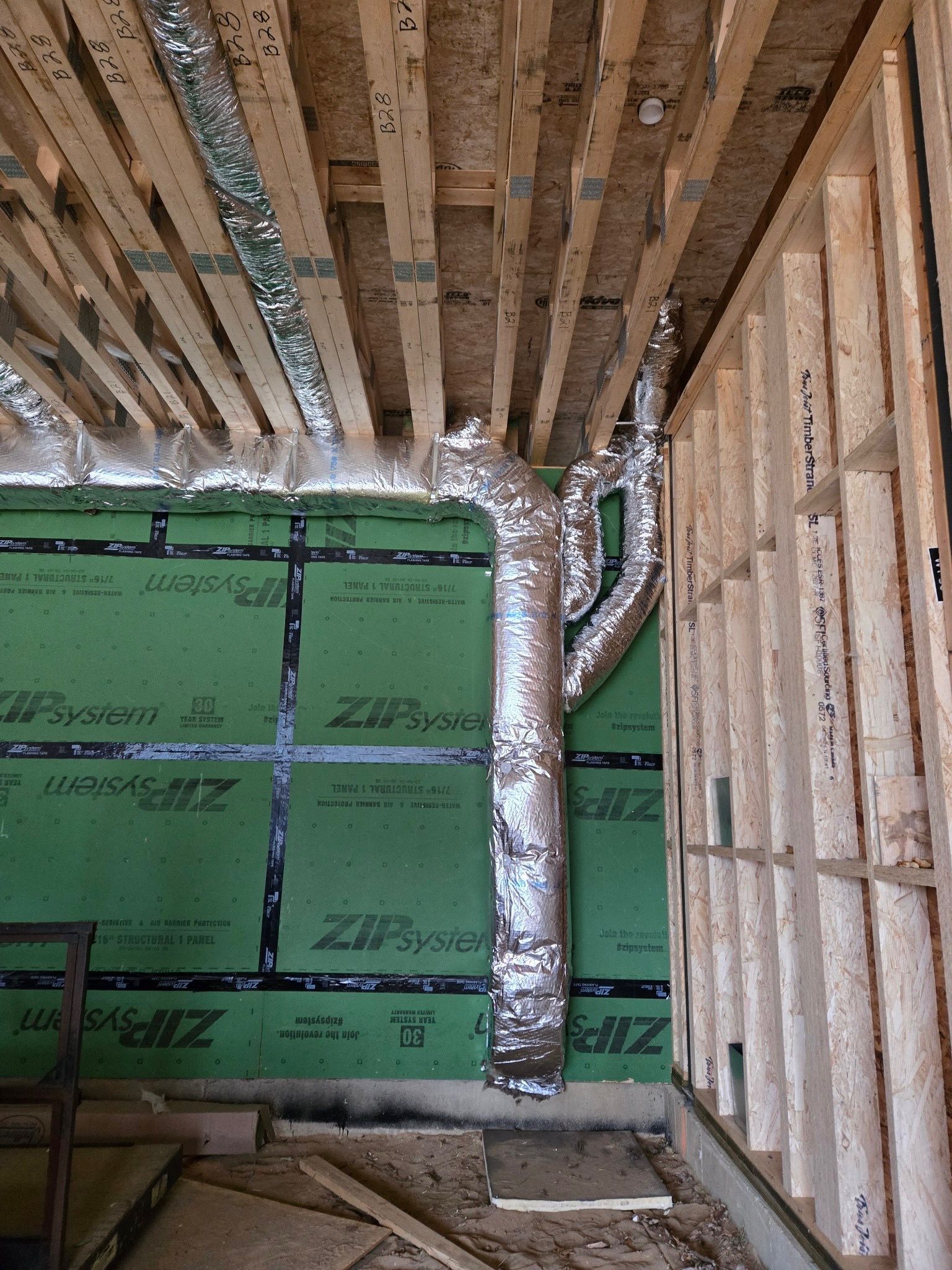 Partially finished room with exposed framing, green insulation, and a silver duct running from floor to ceiling